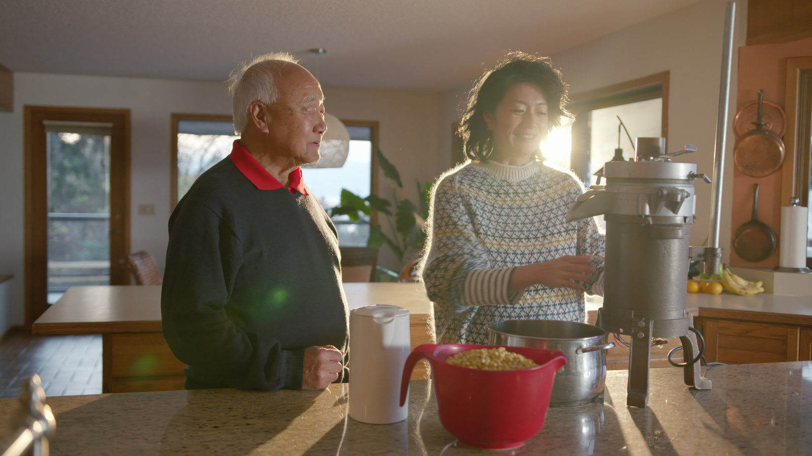 Jackie Kai Ellis and a guest preparing food in a sunlit kitchen