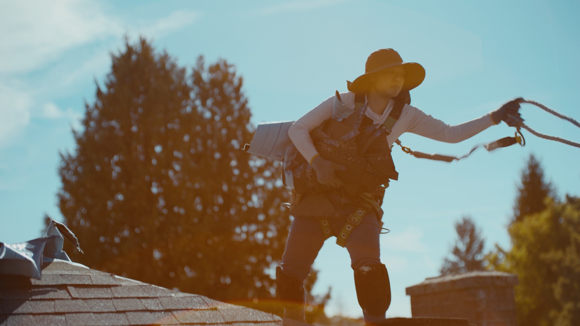 A person in a wide-brimmed hat handling a safety rope on a rooftop